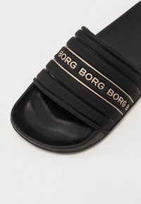 Svart sandaler med skråbånd som har preget "BORG"-tekst og en teksturert, litt blank såle. Flat såledesign.