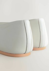 Valkoiset nahka ballerinat, joissa on sileä pinta, pyöreä kärki ja pieni beige pohja. Korostaa kontrastivalkoiset saumat.