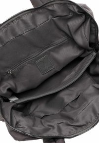 Black nylon bag interior with spacious main compartment, zip pocket, and smooth texture. Features a branded leather tag.