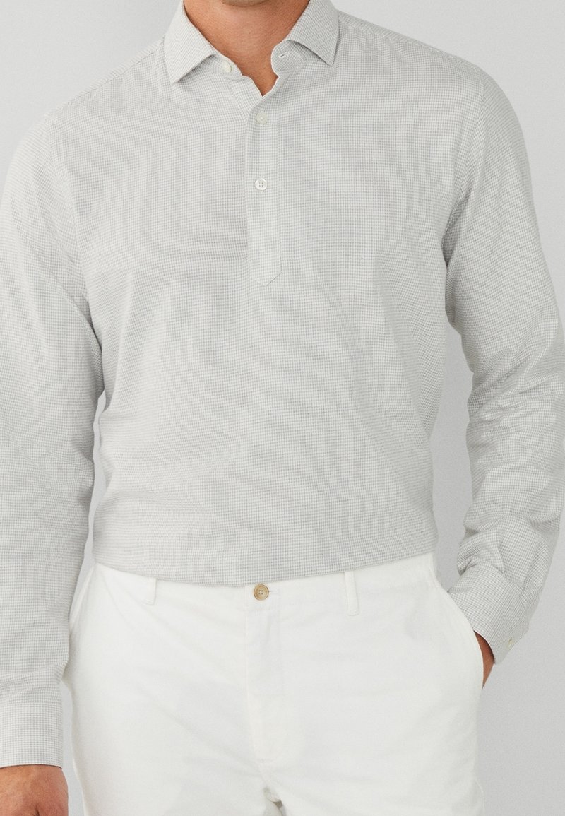 Lange mouw button-up shirt in lichtgrijs met kleine ruiten, voorzien van een puntige kraag en een enkele knopenlijst, gecombineerd met witte broeken.