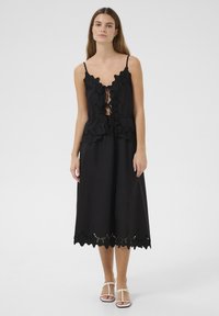 Black dress with a scalloped, embroidered neckline and hem. Features adjustable straps, a loose fit, and delicate cut-out details.