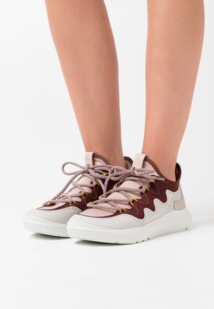 Zapatillas bajas con parte superior de ante burdeos, acentos beiges, suela blanca texturizada y cordones contrastantes con puntas amarillas.