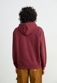 Maroon hoodie with a smooth texture, drawstring hood, and ribbed cuffs and hem. Worn with tan corduroy cargo pants.