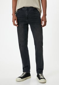 Jeans de mezclilla oscura con un corte recto, que cuentan con cinco bolsillos, trabillas para cinturón y una sutil textura desgastada. Combinados con zapatillas negras.