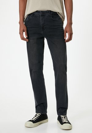 Jeans de mezclilla oscura con un corte recto, que cuentan con cinco bolsillos, trabillas para cinturón y una sutil textura desgastada. Combinados con zapatillas negras.