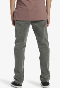 Pantalones rectos grises con tejido ligeramente texturizado, detalles de costura y una cintura. Combinados con zapatillas negras de caña alta.