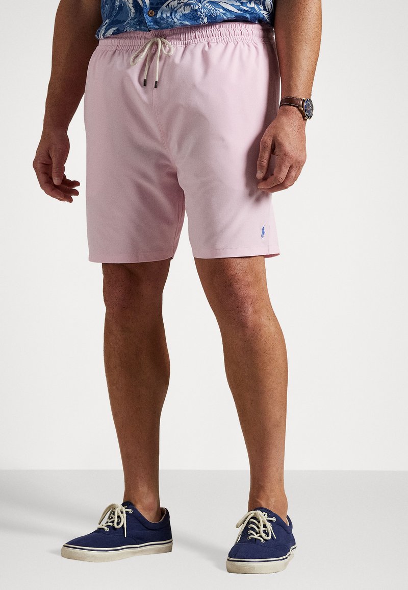 Pantaloni scurți de înot roz deschis cu talie elastică și șnur; logo subtil pe piciorul stâng. Asortați cu pantofi din canavice de culoare albastră închis.