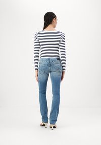 Blue denim jeans with a slim fit, featuring a mid-rise waist, rear pockets, and subtle fading. Paired with a black and white striped long-sleeve top.