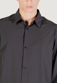 Camicia button-up grigio scuro con colletto classico, texture liscia e bottoni neri. Presenta una vestibilità su misura e un design minimalista.