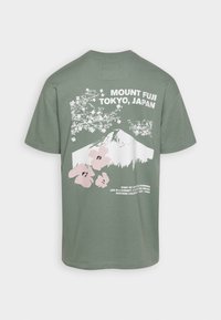 Green t-shirt with white and pink graphic of Mount Fuji, cherry blossoms, and text reading "Mount Fuji Tokyo, Japan" on the back.