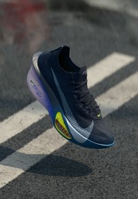 Buty biegowe Nike z czarną, dzianinową cholewką, gradientami w odcieniach niebieskiego i szarości, widoczną poduszką powietrzną oraz jaskrawymi żółtymi akcentami na podeszwie.