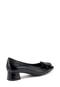 Zapato de tacón negro de cuero con puntera redondeada, lazo decorativo en la parte delantera y un tacón corto y cuadrado. Textura suave, diseño elegante y detalles mínimos.