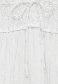 Tissu blanc avec des rayures verticales et des accents texturés, taille froncée avec cordon de serrage, matériau léger et légèrement transparent.