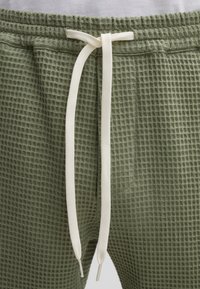 Groene joggers met een waffle-textuur, voorzien van een elastische tailleband en een crèmekleurige trekkoord voor verstelbaarheid. Eenvoudig ontwerp, geschikt voor casual kleding.
