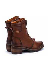 Bottines en cuir marron avec un bout rond, un laçage à l'avant et un talon en bois moyen. Présente des accents de couture et un col rembourré.