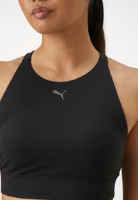 Svart idrettstopp med høy hals laget av glatt stoff, med minimalistisk grå Puma-logo foran, uten mønstre eller aksenter.