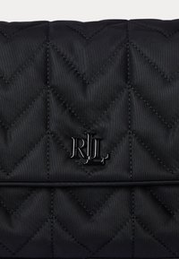 Črna prešita torbica s ševron vzorcem, ki ima kovinski RLL logo kot dekoracijo. Material se zdi gladek z sijajno površino.