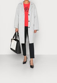 Gray wool coat with large buttons, red top with black script, black slim trousers, black heels, and a two-tone black and white tote bag.