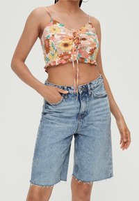 Top corto floral en colores pastel con lazos ajustables y dobladillo con volantes, combinado con pantalones cortos de mezclilla azul claro de cintura alta y bordes deshilachados.