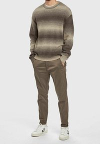 Stickad tröja med gradientnyanser från ljus till mörkbrun, ribbad halsringning och ärmslut. Parat med beige byxor och vita sneakers med svarta accenter.