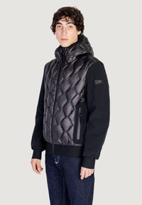 Giacca imbottita con cappuccio, caratterizzata da un frontale trapuntato nero lucido, maniche matte nere in contrasto e tasche con zip.