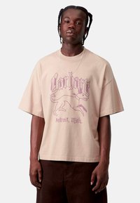 T-shirt oversize beige in cotone con una grafica viola di un cane e la scritta "Carhartt Detroit, Mich." Maniche corte, vestibilità rilassata.