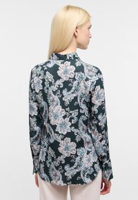 Blusa a maniche lunghe in seta verde scuro con motivo floreale e paisley in tonalità pastello. Presenta un colletto classico e un orlo curvo.
