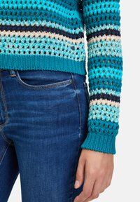Pull en crochet aux nuances de turquoise, présentant des motifs rayés avec des accents marine et crème. Ourlet et poignets côtelés ; texture légère.