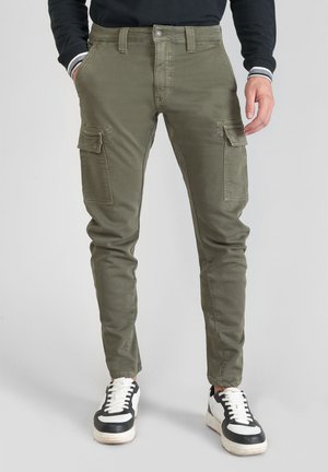 Olive green cargo pants with side pockets, slim-fit design, and reinforced stitching. Paired with black and white sneakers.