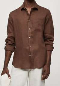 Chemise en lin marron avec boutons, une poche, manches longues retroussées et boutons couleur argent. Texture légère pour une meilleure respirabilité.