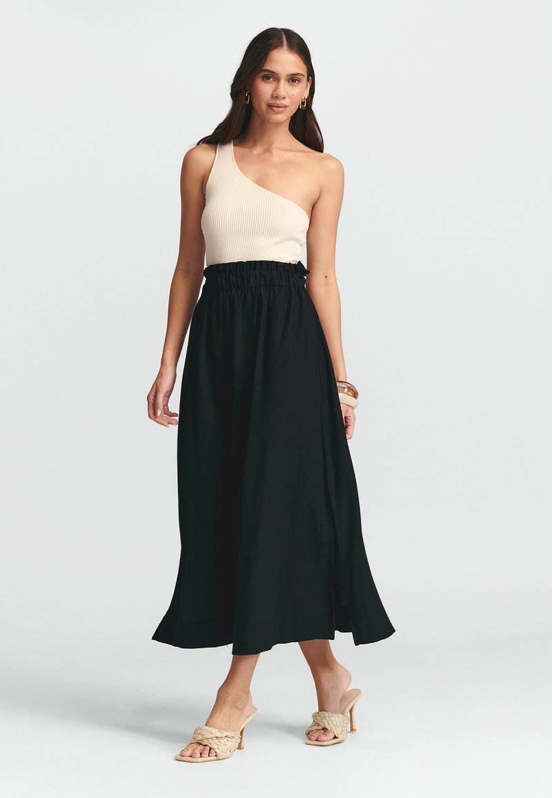 Čierna maxi sukňa s elastickým pásom, doplnená krémovým rebrovaným topom s jedným ramienkom. Mäkká látka a splývavá silueta.
