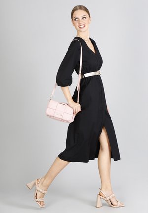 Abito nero con scollatura a V, maniche a palloncino e uno spacco laterale, abbinato a una borsa a tracolla rosa e sandali con tacco bloccato beige.