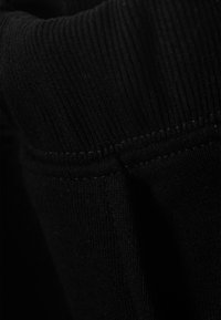 Μαύρο βαμβακερό ύφασμα με ριμπ υφή, εμφανή ραφές. Κοντινό πλάνο της άκρης του ρούχου, που αναδεικνύει την απαλότητα και την ελαστικότητά του.