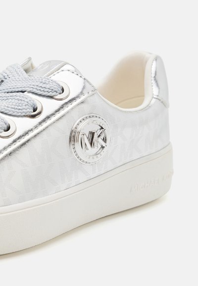 Baskets argentées avec une tige brillante, présentant un motif monogramme subtil, un accent de logo rond et des lacets gris clair sur une semelle en caoutchouc blanche.