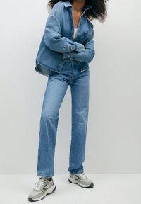 Giacca di jeans azzurra chiara con vestibilità comoda e chiusura a bottoni, abbinata a jeans azzurri chiari e sneakers grigie.