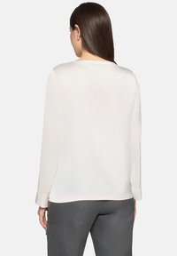 Langærmet, blød hvid bluse med rund halsudskæring og manchetærmer, kombineret med grå, skræddersyede bukser. Glat tekstur, enkelt design.