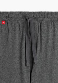 Szare dresy z elastycznym pasem i sznurkiem do regulacji. Posiadają małą czerwoną metkę oraz miękką, teksturowaną tkaninę.