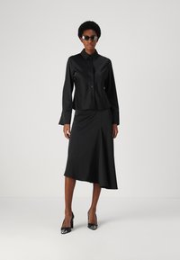 Czarna satynowa koszula zapinana na guziki zestawiona z dopasowaną spódnicą w kształcie litery A. Stylizacja charakteryzuje się eleganckim krojem, długimi rękawami i bocznym rozcięciem.