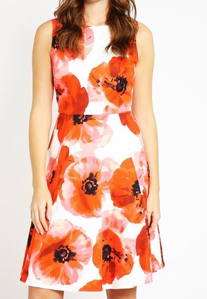 Biała sukienka bez rękawów z dużymi, wyrazistymi nadrukami maków w kolorach pomarańczowym i różowym, dopasowana w talii, noszona przez stojącą osobę.