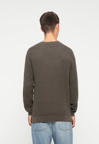 Suéter de punto gris oscuro texturizado con cuello redondo y puños acanalados, combinado con jeans de color azul claro, visto desde la espalda.