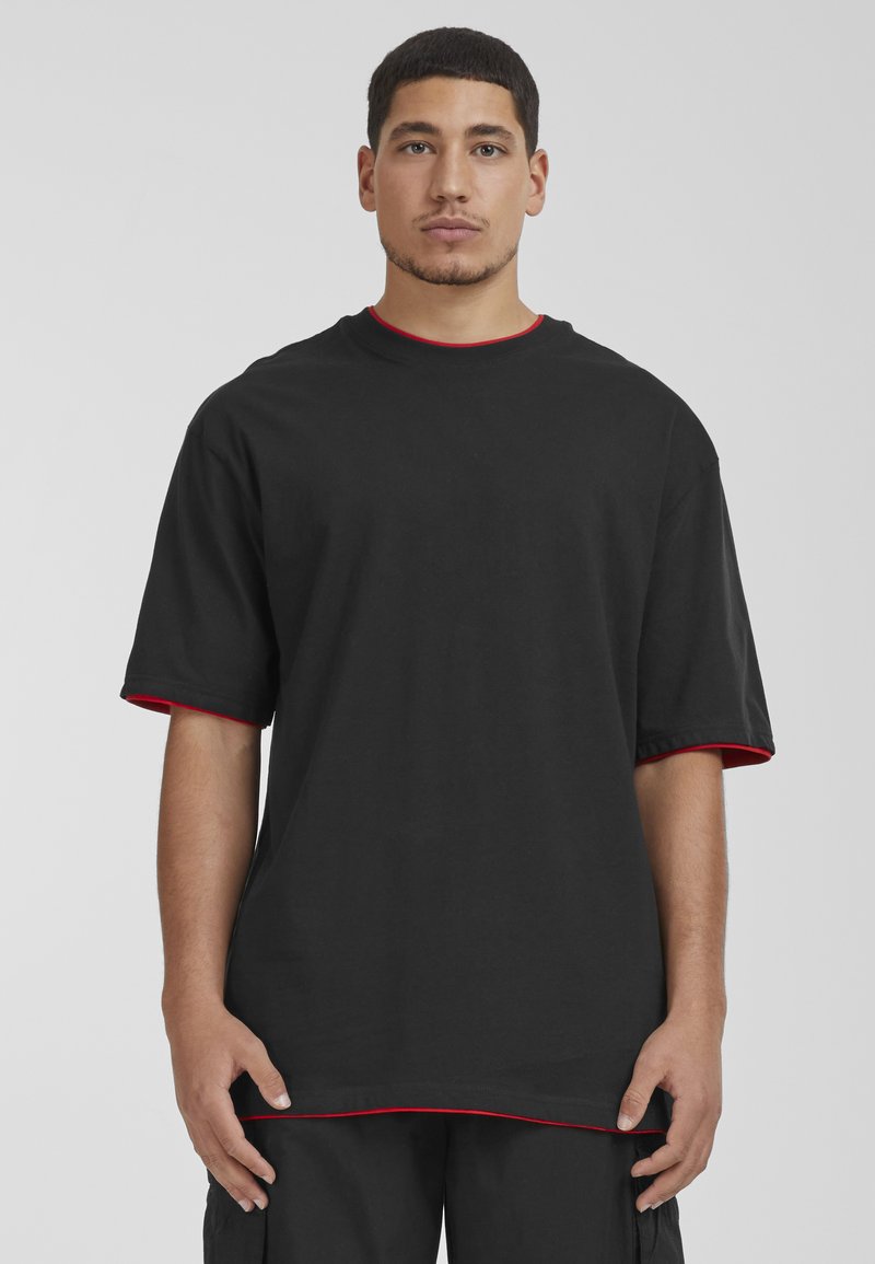 Camiseta negra de manga corta con detalles en rojo en el cuello y las mangas. Hecha de algodón, presenta un corte relajado y un dobladillo recto.