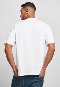 T-shirt bianco in cotone con maniche corte, vestibilità rilassata e scollo rotondo, che mostra una trama liscia e dettagli di design minimi.