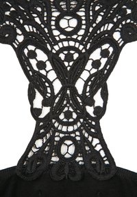 Svart spets tyg har en intrikat, blommig design med öglor och cirklar, kombinerat med solid svart material för stöd.