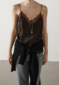 Brun satinkamisol med spetskant och tunna band, lager-på-lager med en svart tröja knuten i midjan, kombinerad med grå denimjeans.