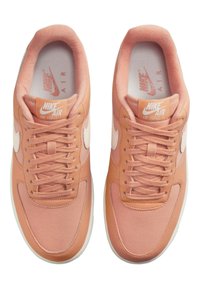 Nike Air Force 1-skor, med en mjuk persikofärgad läderöverdel, tonmatchande snören och en kontrasterande vit swoosh-logotyp.