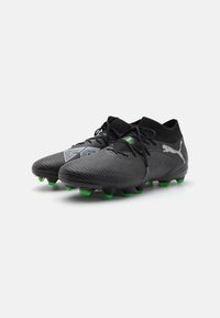 Black soccer cleats with a textured upper, featuring green studded soles and a gray design element on the side. Laces and ankle support included.