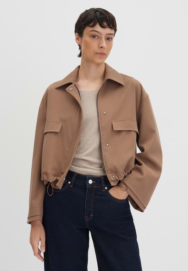 Bruine cropped jas van zacht materiaal, met een opstaande kraag, voorzakken en een ingezoomde taille. Gekocht over een beige top en donkere jeans.