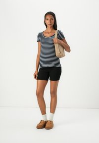 Ναυτικό και λευκό ρι�γέ κοντομάνικο μπλουζάκι συνδυασμένο με μαύρες βερμούδες. Μπεζ τσάντα στον έναν ώμο, καφέ παντόφλες, λευκές κάλτσες.