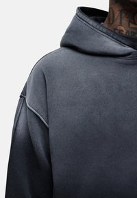 Felpa con cappuccio grigio scuro caratterizzata da un tessuto testurizzato, vestibilità comoda e un grande cappuccio per una buona copertura. Nessun motivo visibile o dettagli aggiuntivi.