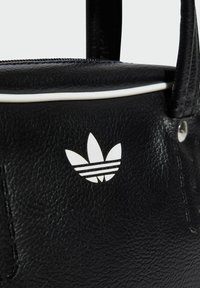 Black leather handbag with white accent piping. Features iconic white three-leaf logo and zipper details. Textured surface with stitching.